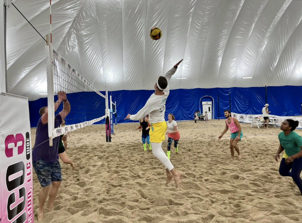 A player jumps to hit the ball over the net on a sand volleyball court