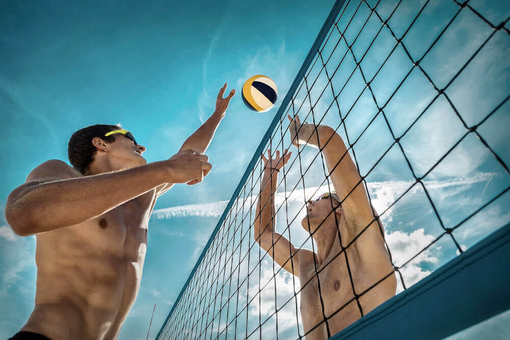 Two male beach volleyball players jumping at the net