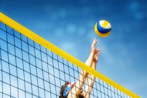 Beach volleyball player jumping to hit ball above net