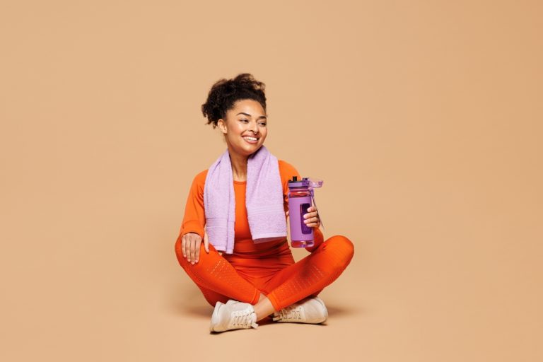 Woman in athletic wear sitting on the floor with a water bottle and towel
