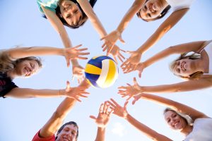 group of young adults smiling and playing sand volleyball