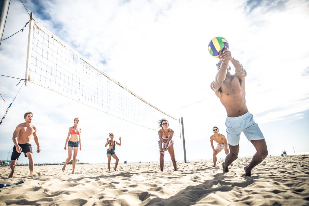 Co-ed adult sand volleyball league game on a sunny day, with players diving and setting on the sand