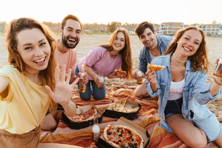Group of friends enjoying pizza and drinks together on the sand