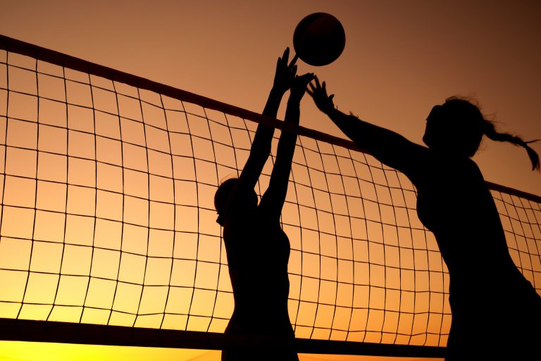Silhouette of sand volleyball players jumping at the net during a sunset match