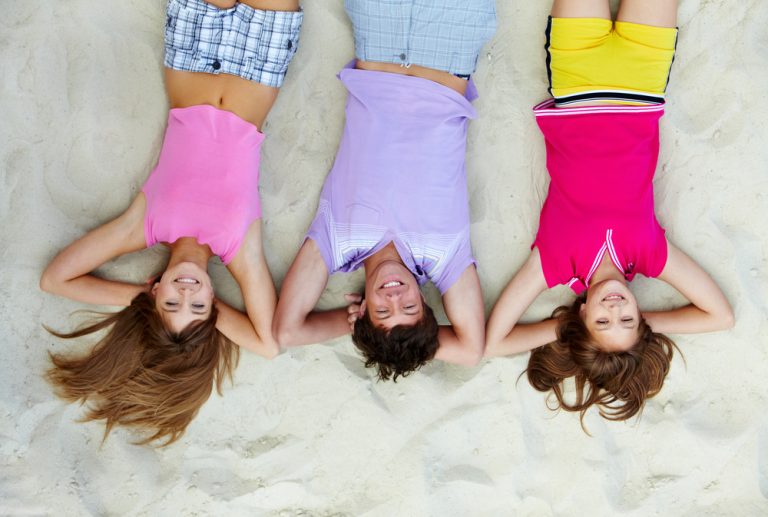 Teenagers smiling on the sand after a fun game of beach volleyball